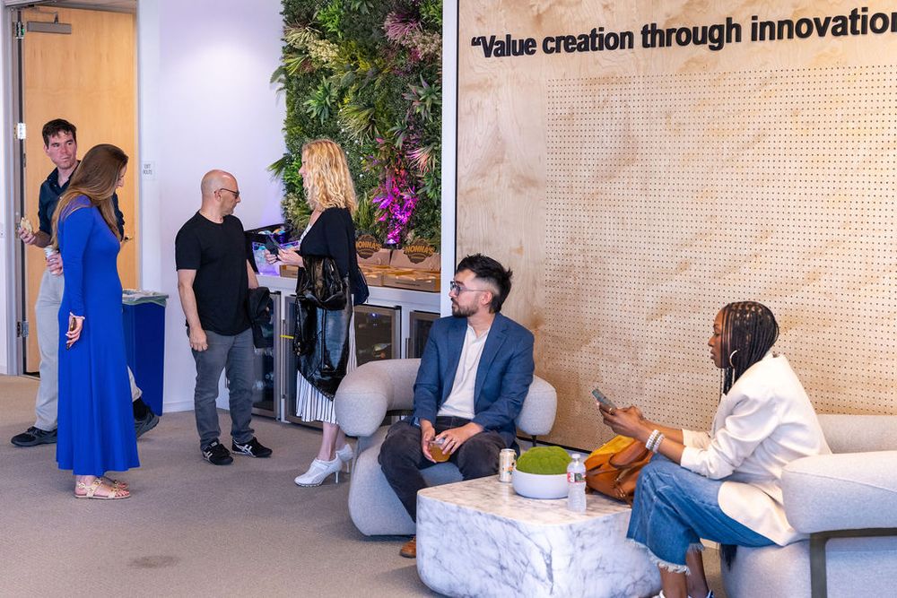 Professionals networking in a modern office lobby with a 'Value creation through innovation' wall and lush greenery.