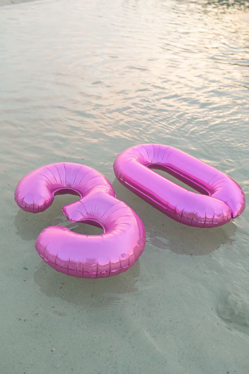 Pink inflatable number 30 balloons floating in shallow water, perfect for a 30th birthday beach celebration.