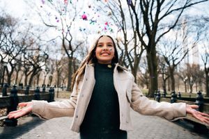 Person spreads arms wide with joy under confetti in winter park setting.