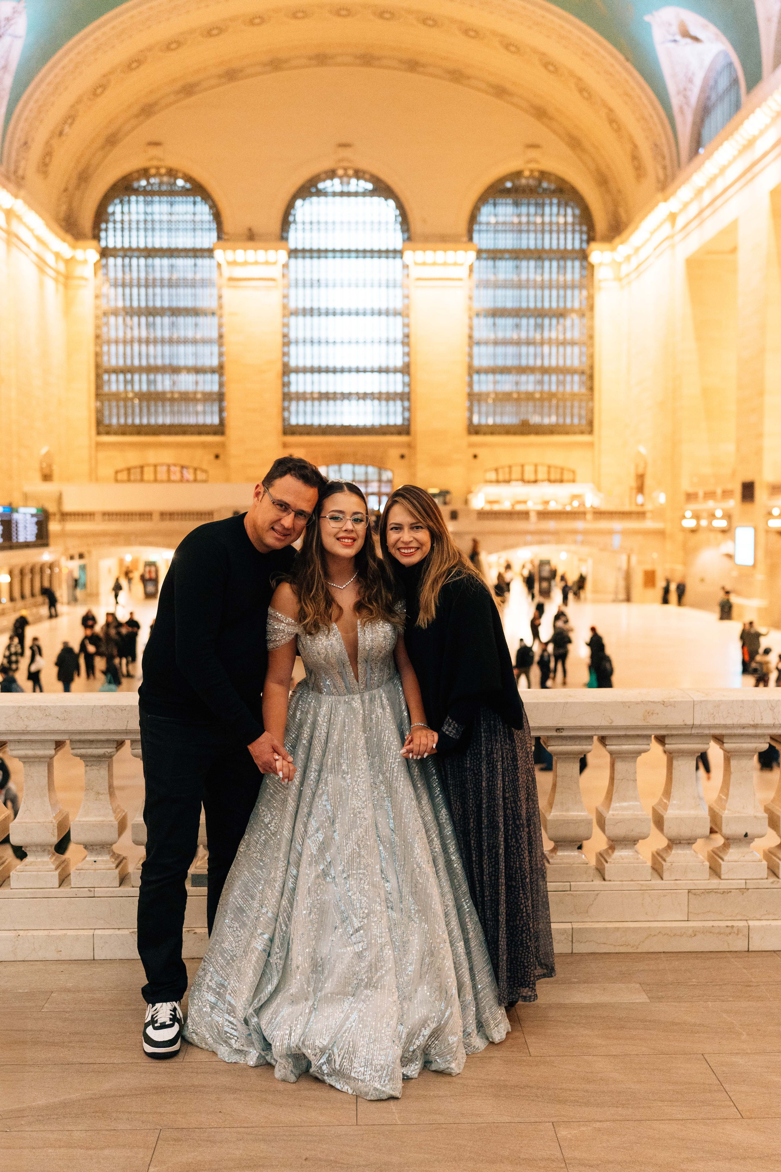 Three people posing together in Grand Central Terminal, NYC, with woman in silver ball gown.