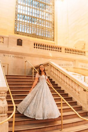 A silver sequined ball gown sparkles on the grand marble staircase of an elegant historic building.