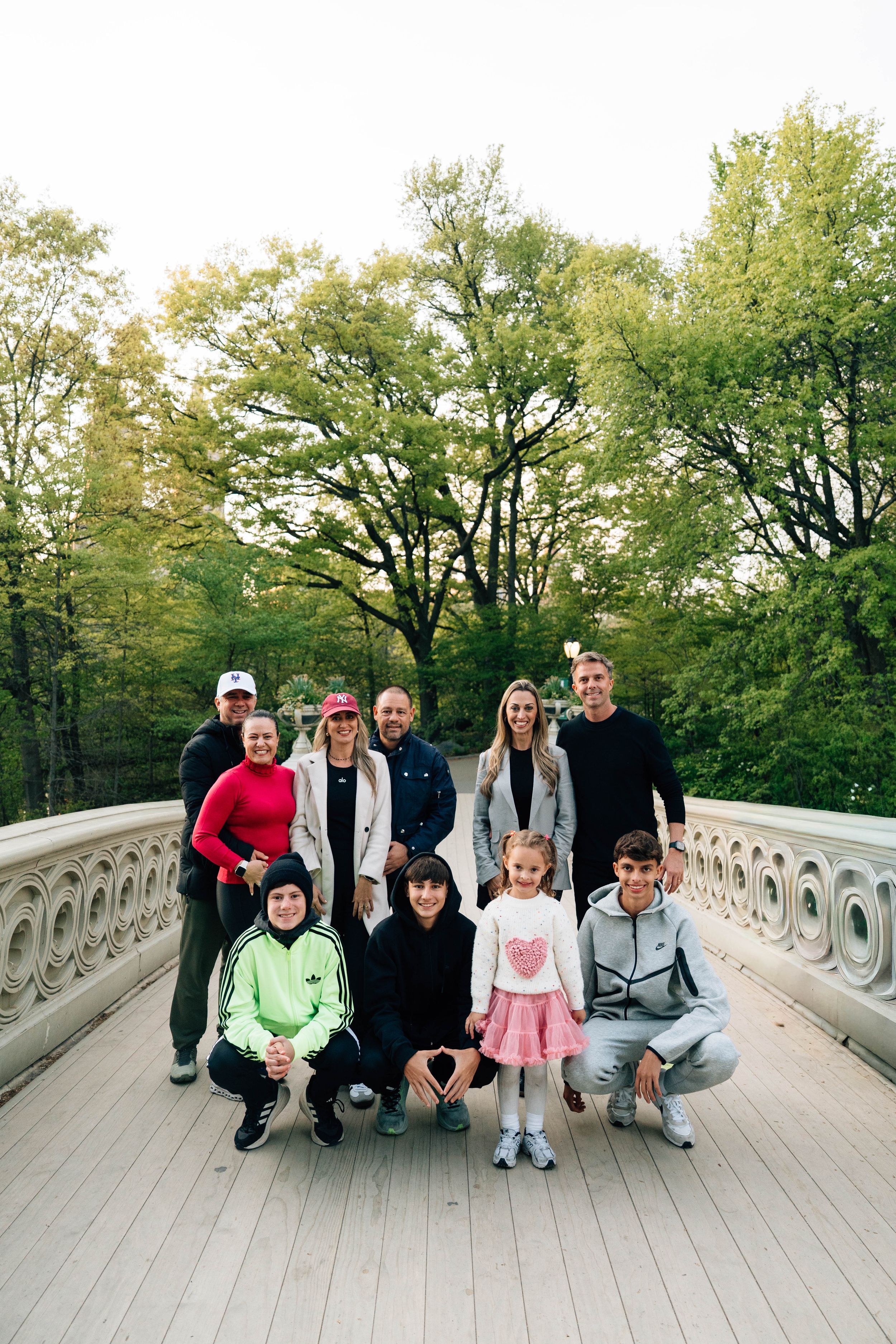 Family group photo on a decorative bridge in Central Park, surrounded by lush green trees in autumn.