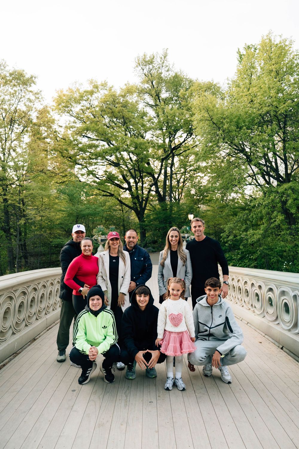 Family group photo on a decorative bridge in Central Park, surrounded by lush green trees in autumn.