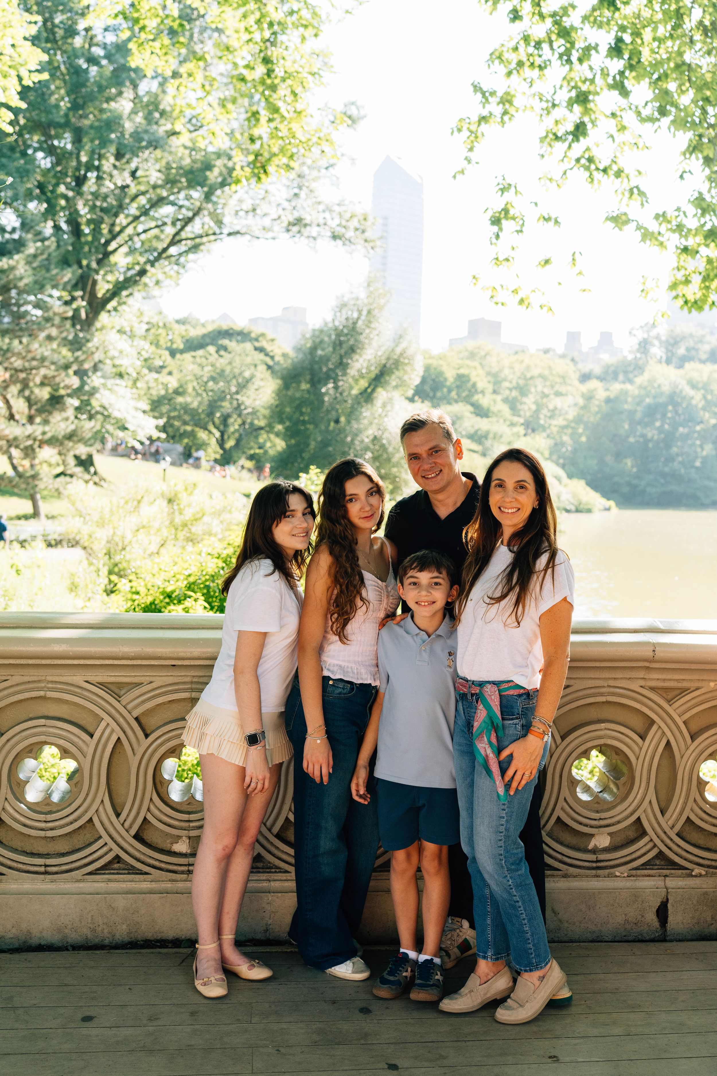 Family of five posing together on a bridge in Central Park, NYC, on a sunny summer day.