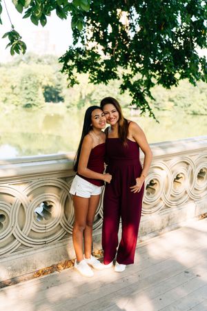 Two young women in matching burgundy outfits pose together on a stone bridge in Central Park, New York.