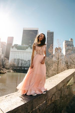 Person in flowing peach gown posing against Central Park and NYC skyline backdrop.