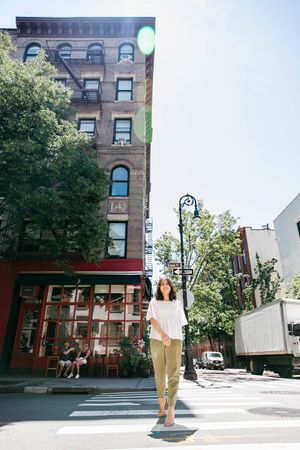 Person walking on a New York City street with historic brownstone buildings and storefronts.