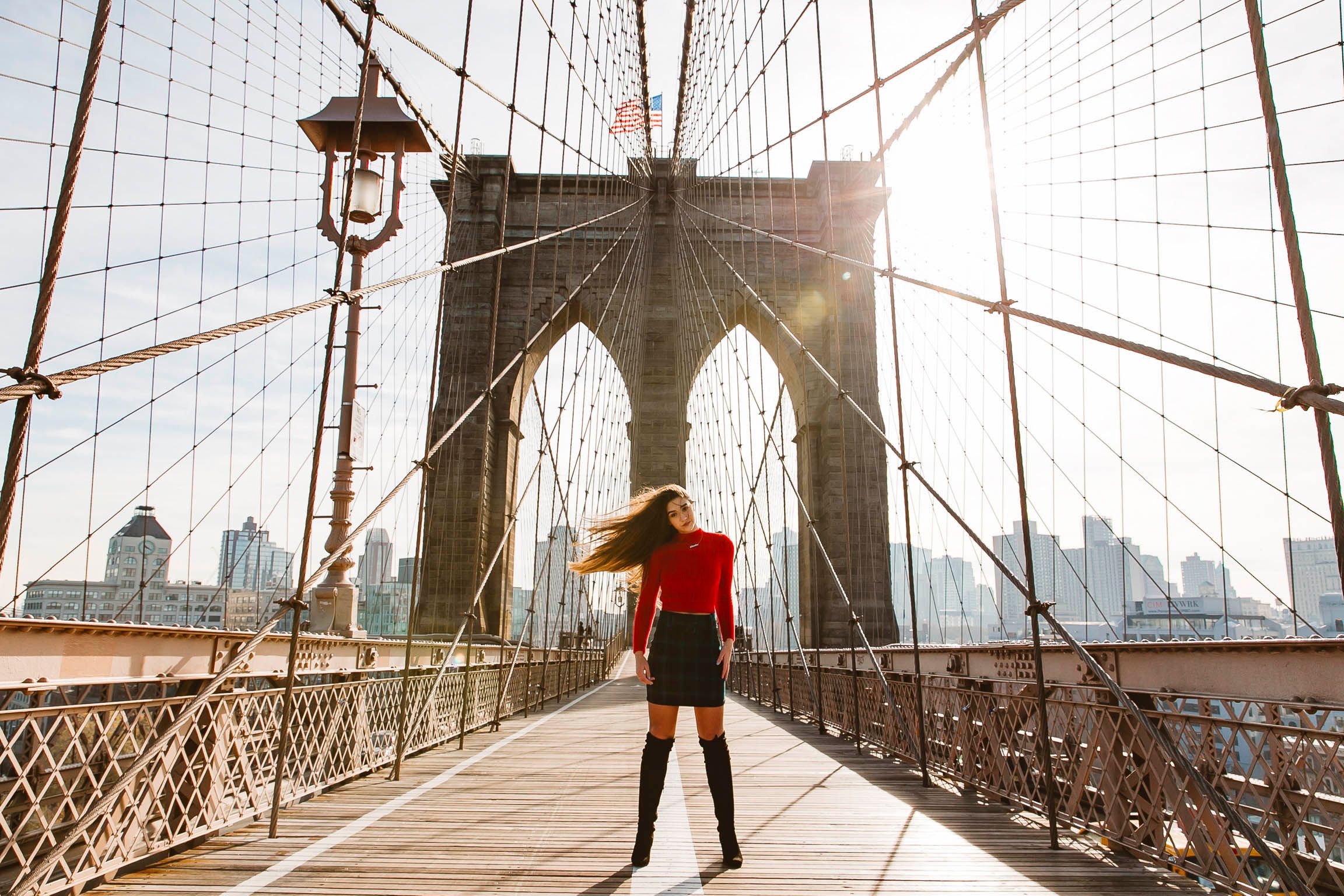 Silhouette standing on the historic Brooklyn Bridge with Manhattan skyline in background.