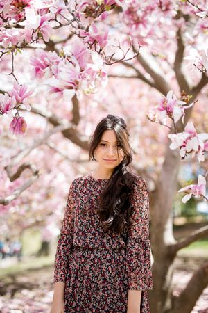 Spring scene with blooming pink magnolia flowers framing figure in floral dress.