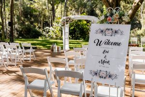 Outdoor wedding ceremony setup with white chairs and a Welcome sign for Eri and Mark surrounded by lush greenery.