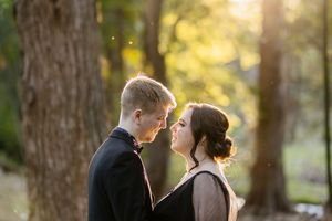 Couple sharing a romantic moment outdoors, bathed in golden sunlight filtering through trees in a forest setting.