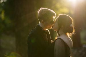 Couple sharing a tender kiss in golden sunlight filtering through trees.