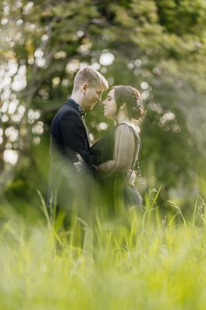Romantic couple embracing in lush green meadow with sunlit trees, sharing an intimate moment outdoors.