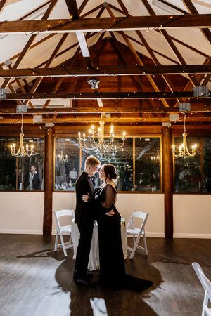 Couple sharing romantic first dance in elegant rustic wedding venue with chandeliers and exposed wooden beams.