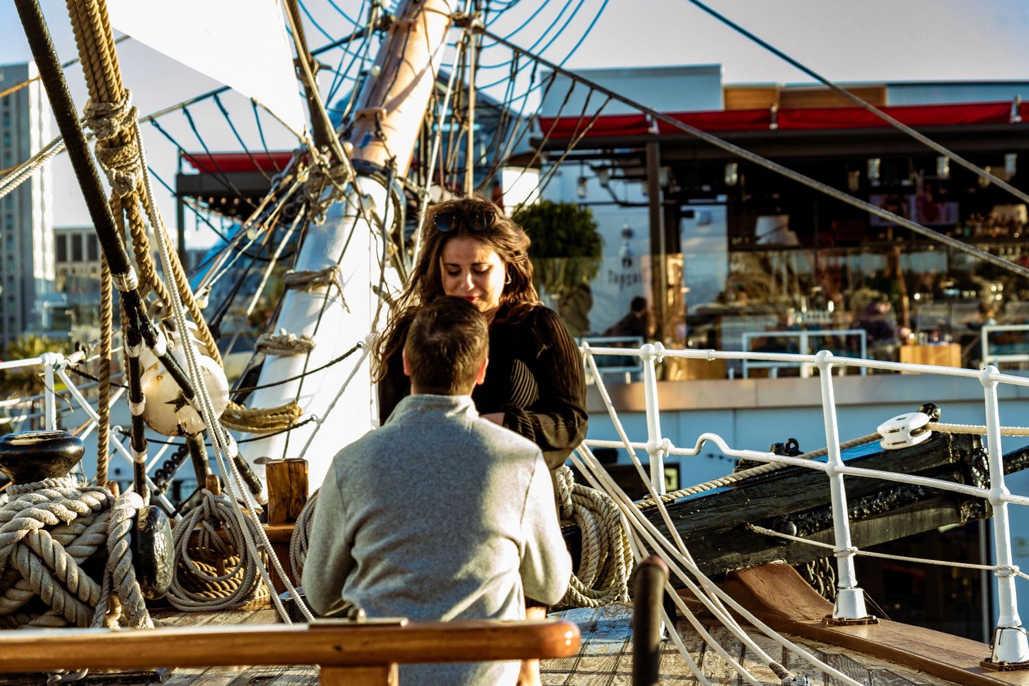 A person in a floral dress officiates a wedding ceremony on a boat deck as a couple embraces.