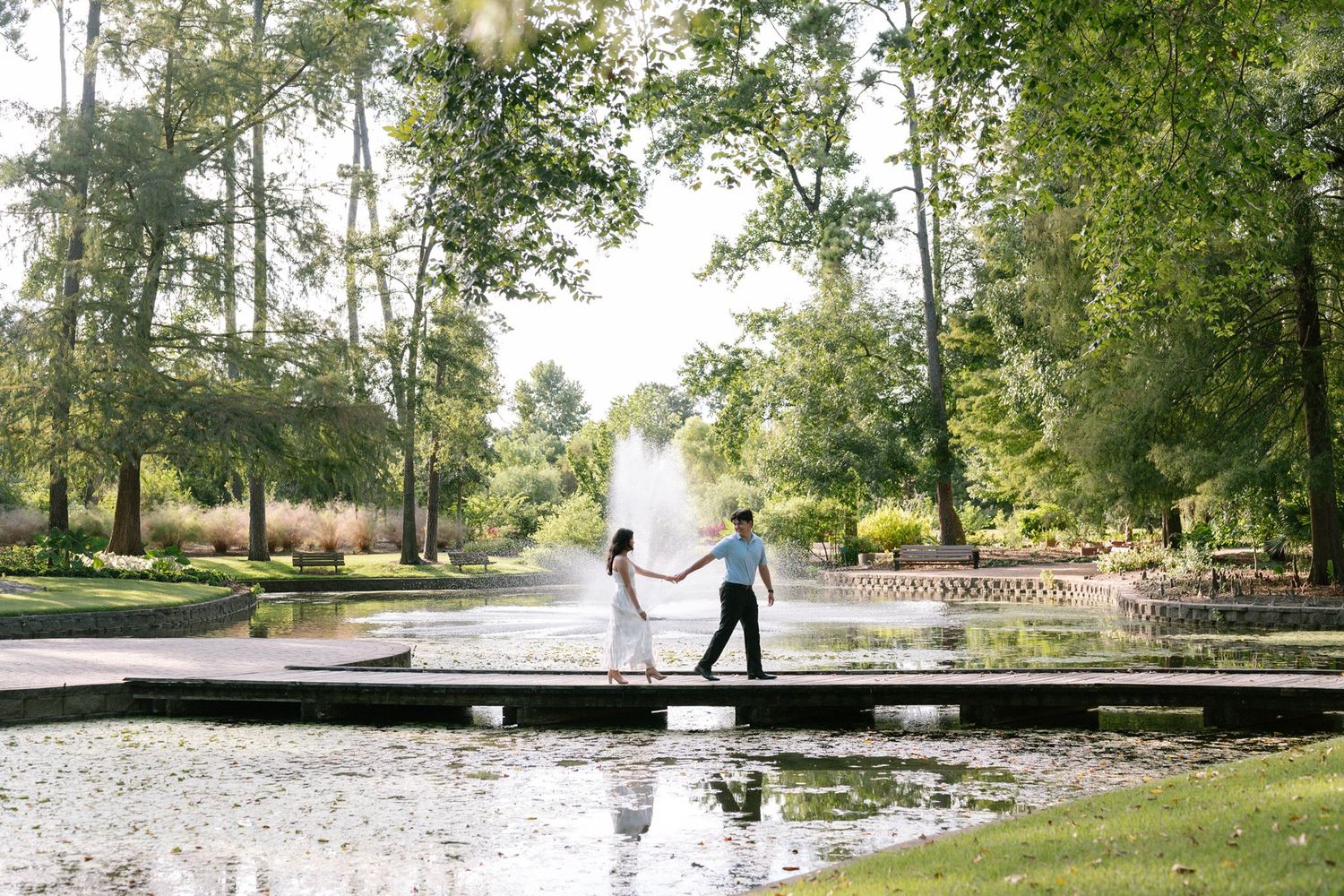 Couple holding hands walking across a bridge over a pond at Mercer Botanic Gardens in Spring Texas