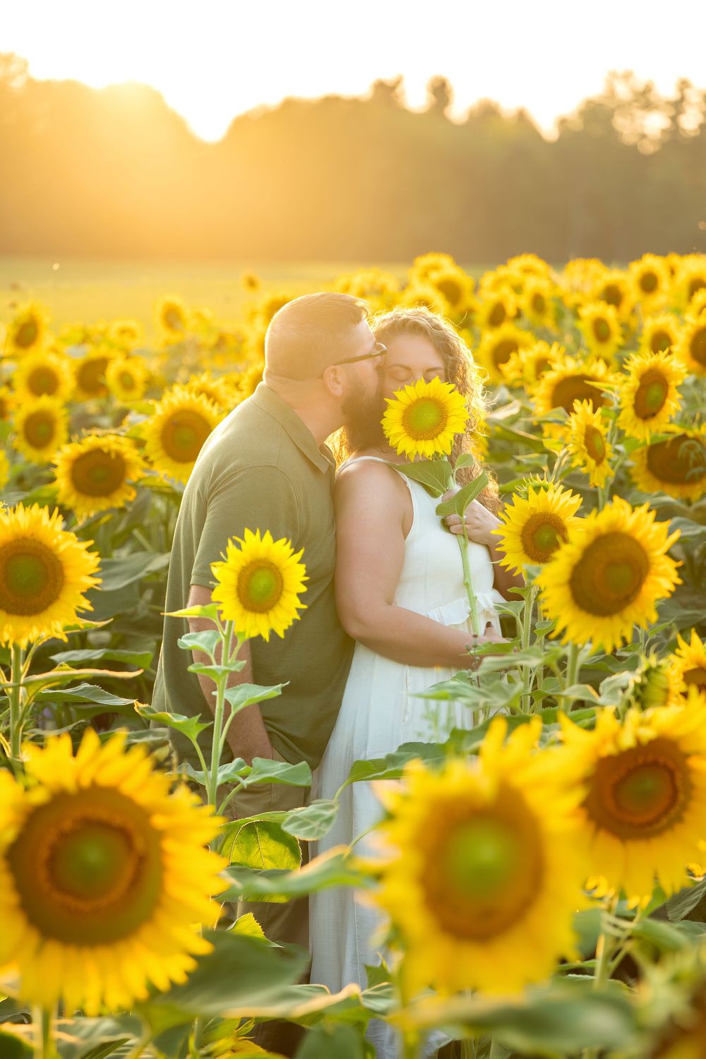 Couple sharing a kiss in a vibrant sunflower field at sunset.