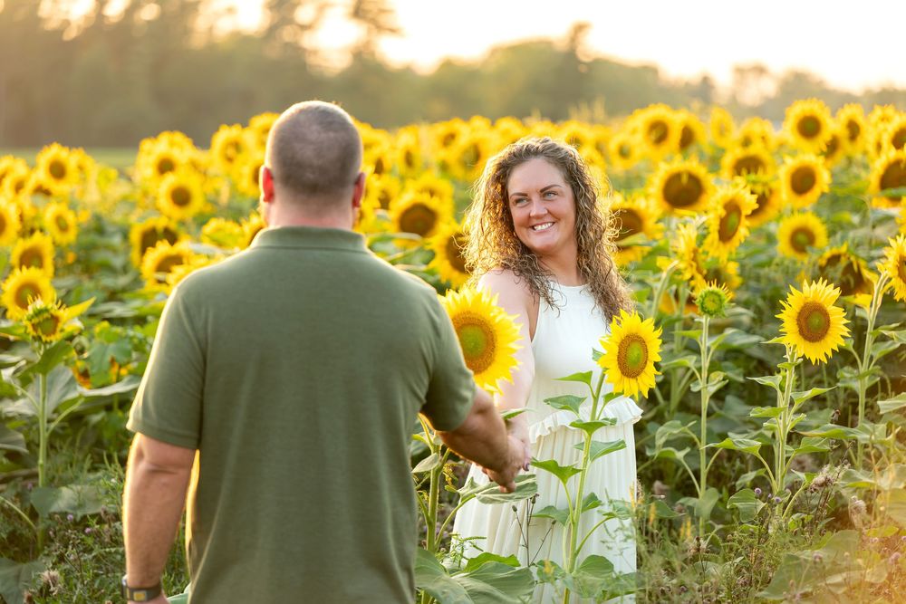 Couple holding hands and smiling in a vibrant sunflower field at golden hour.