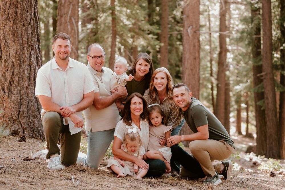 Family of eight posing together in a pine forest, smiling for a professional outdoor portrait photo.