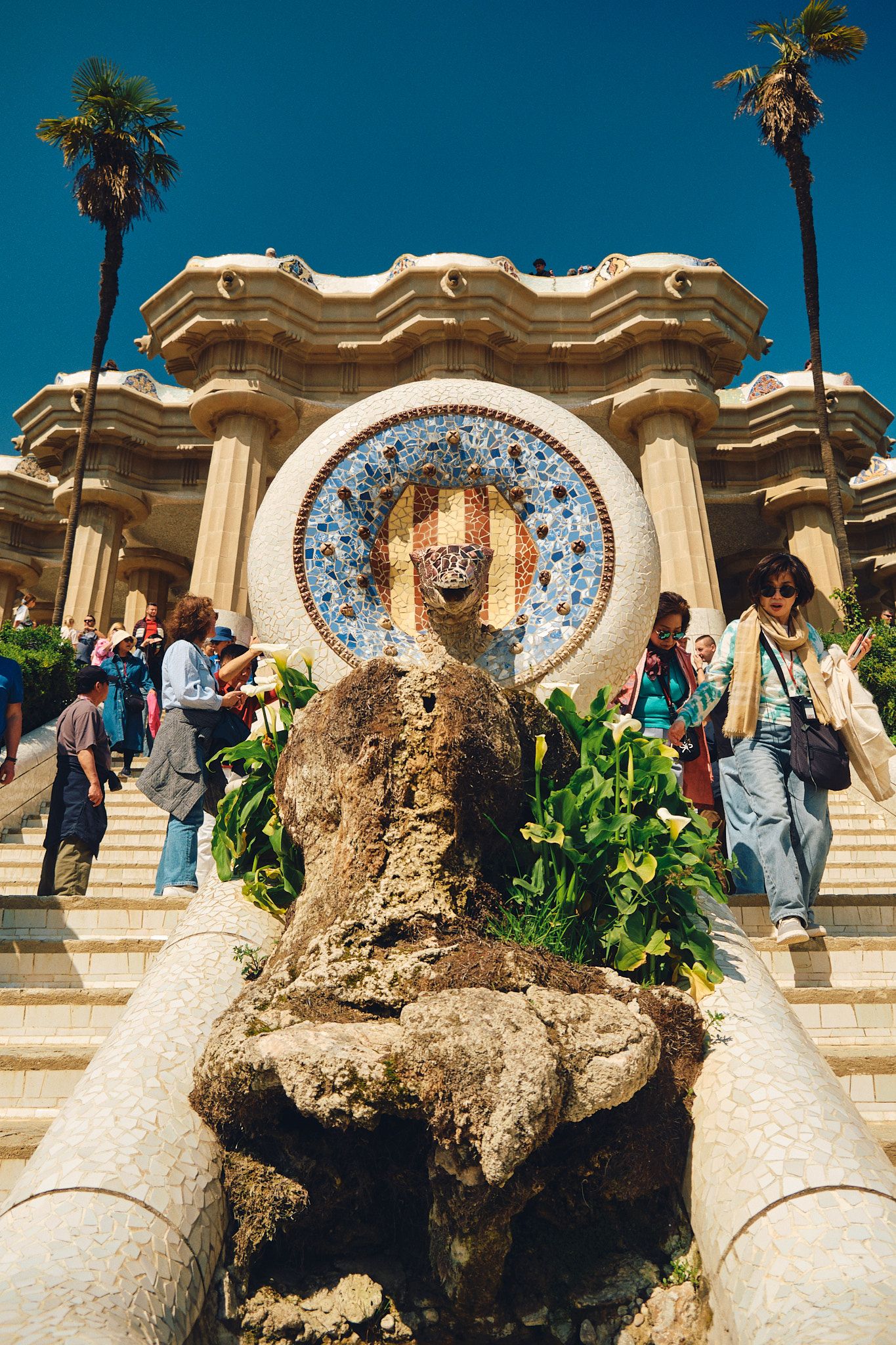 Tourists explore Park Guell's iconic mosaic medallion fountain and grand staircase in Barcelona, Spain.