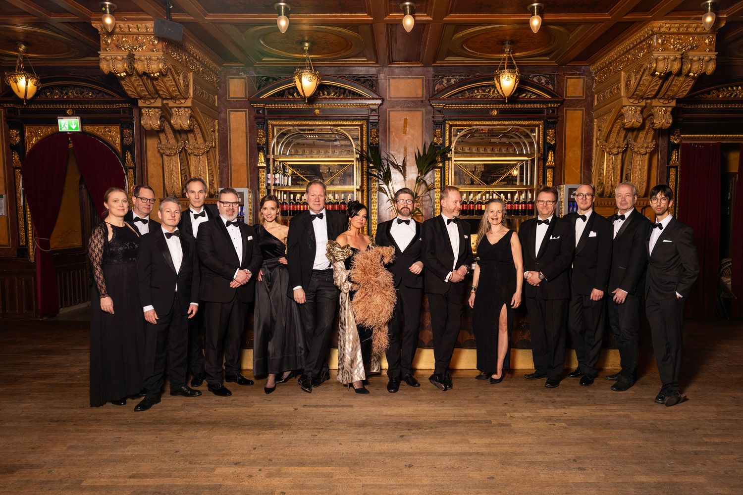 Large group of elegantly dressed guests posing together in ornate ballroom at formal gala.