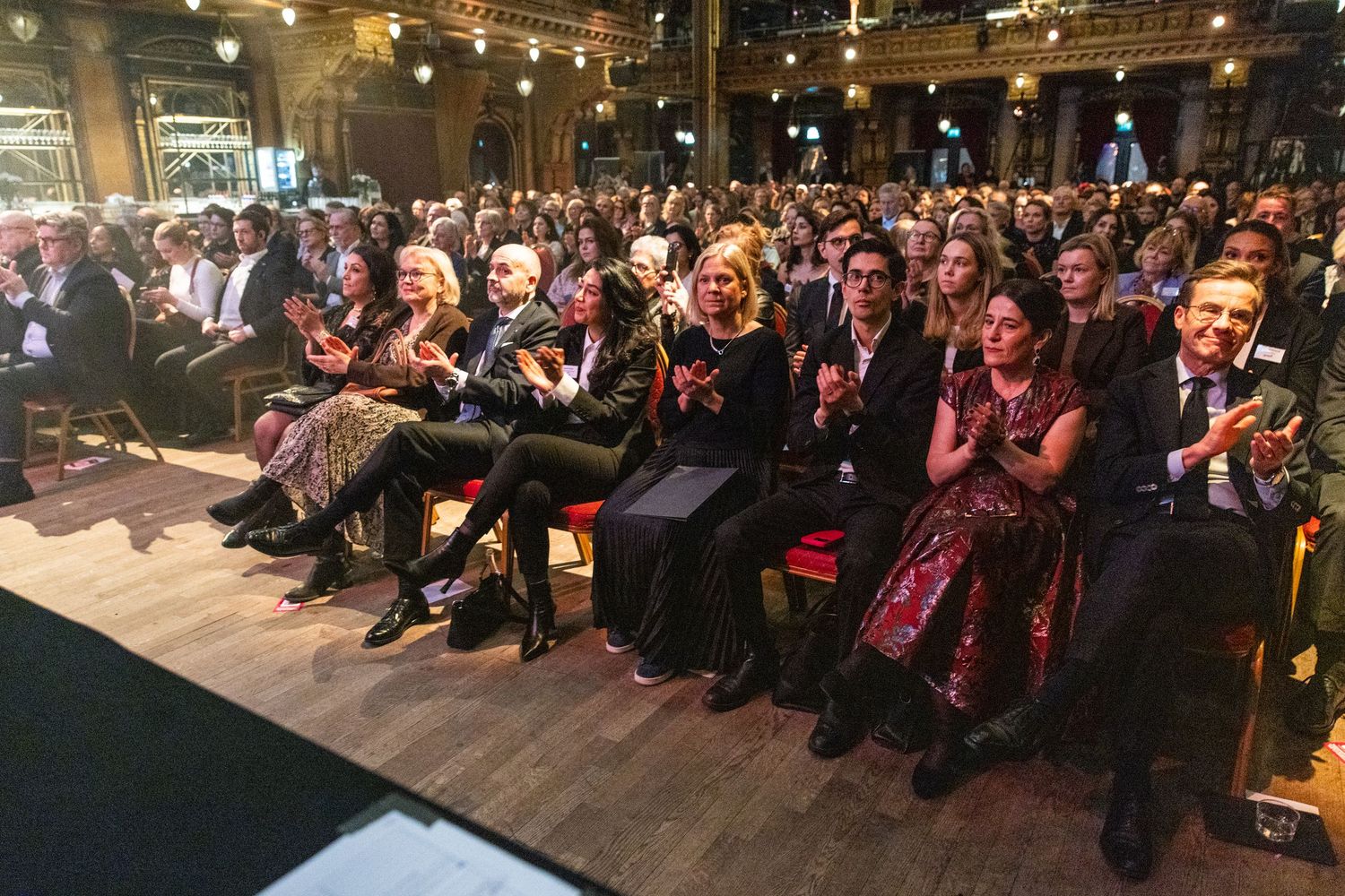 A large audience applauding at a formal event held in an ornate historic venue.