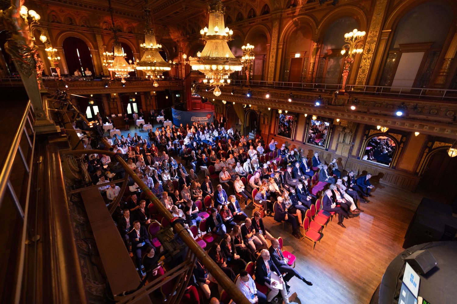 Aerial view of a packed audience in a grand ornate ballroom during a live event.