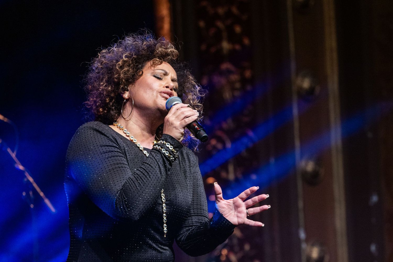 A female singer performing on stage with blue stage lighting at a live event.