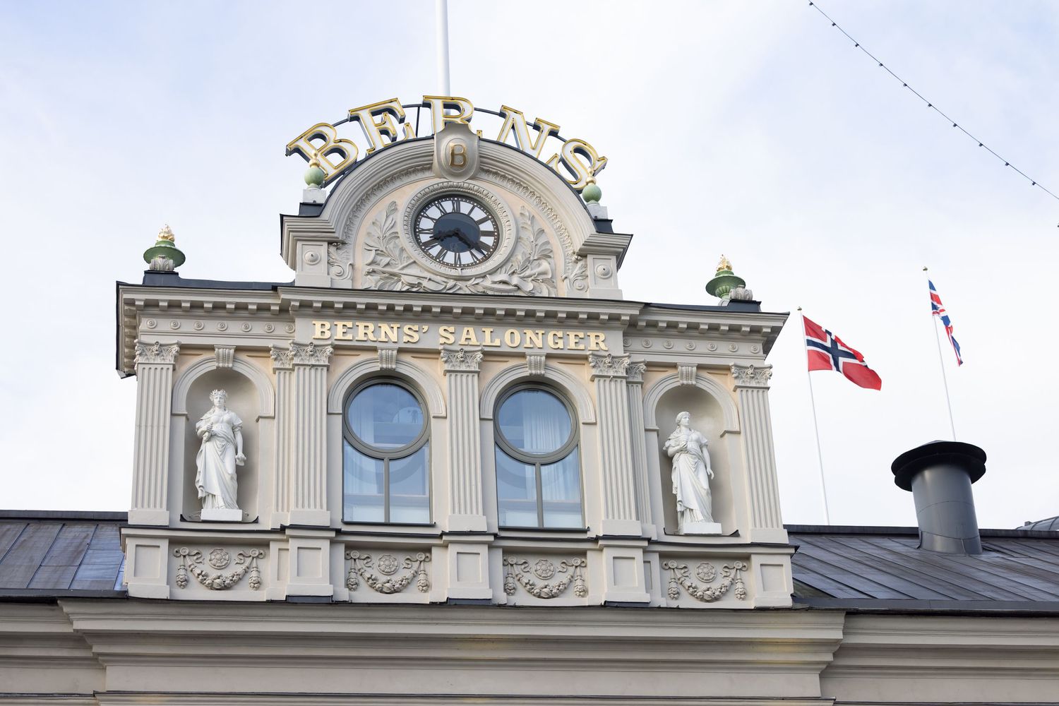 Berns Salonger historic building facade with golden lettering, clock, and Norwegian flag in Stockholm.