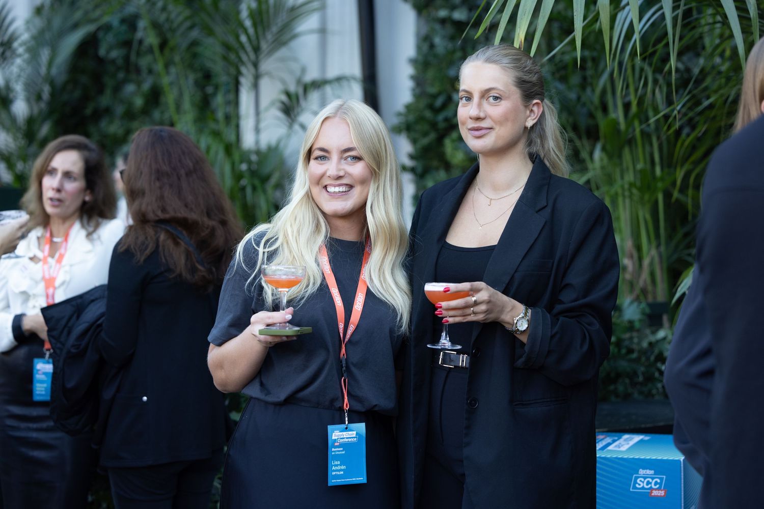 Two women in black attire holding cocktails at a formal networking event.