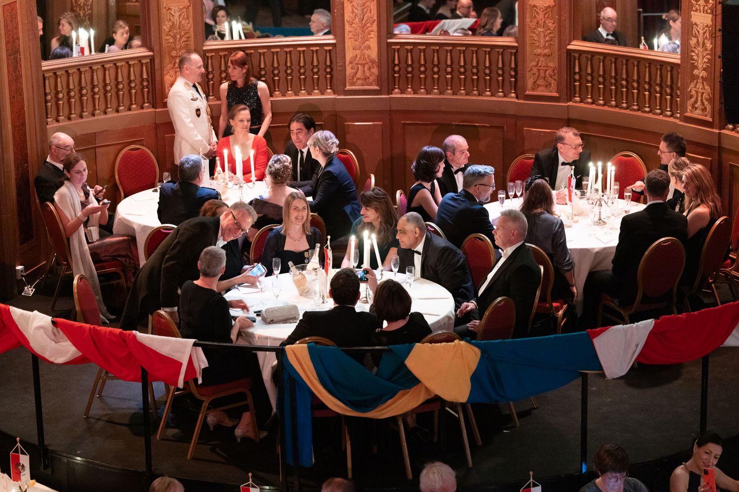 Guests dining at candlelit round tables in a grand ornate ballroom during gala dinner.