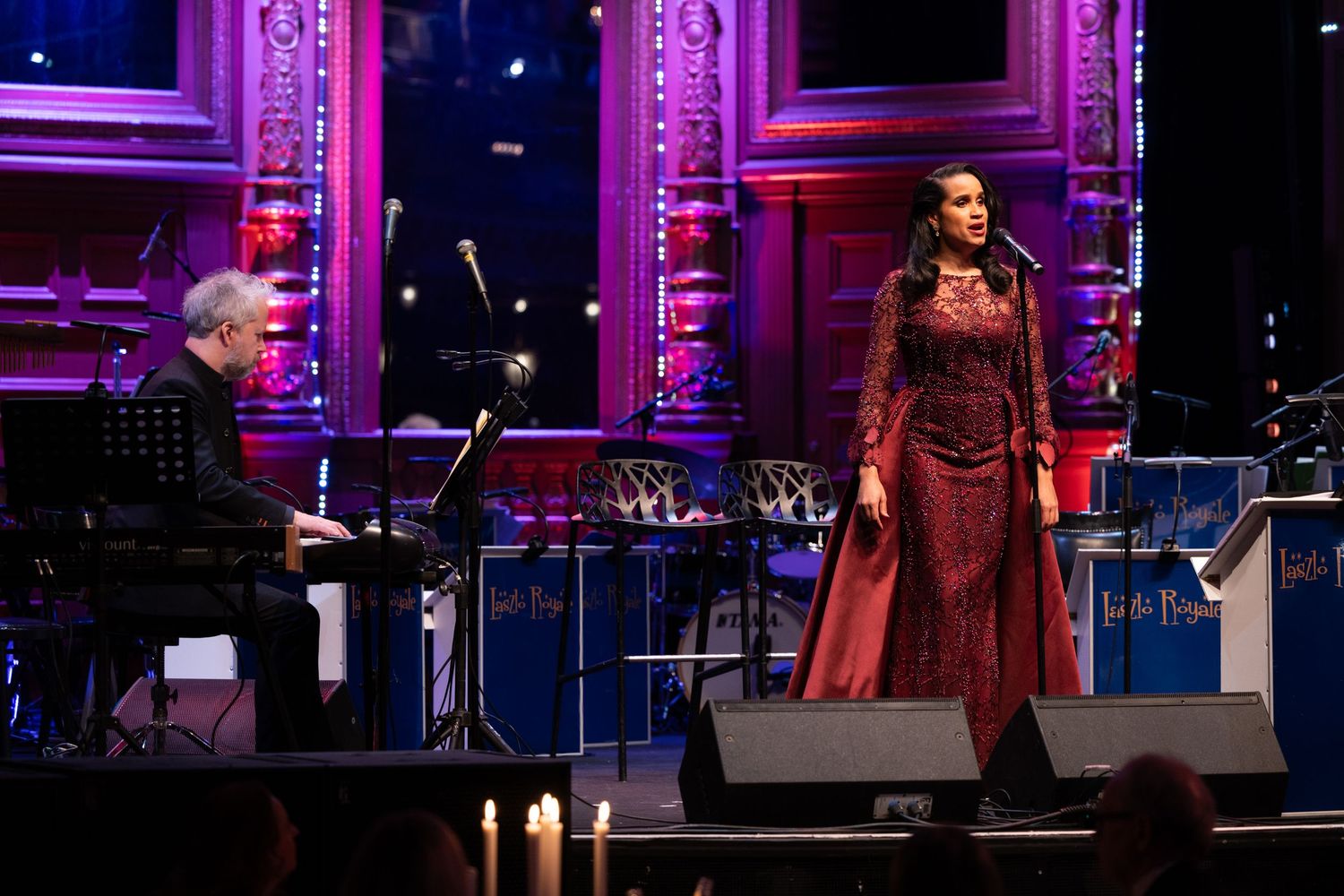 Female singer in red gown performing on stage with pianist at a formal gala event.