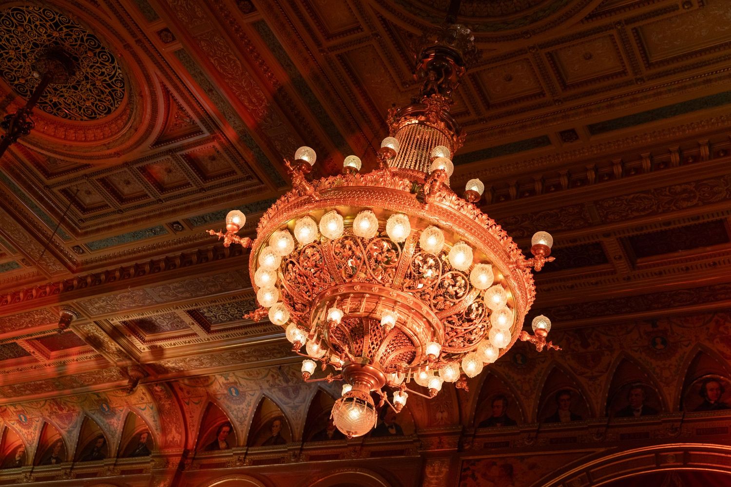 Ornate golden chandelier with globe lights in an elegant historic ballroom ceiling.
