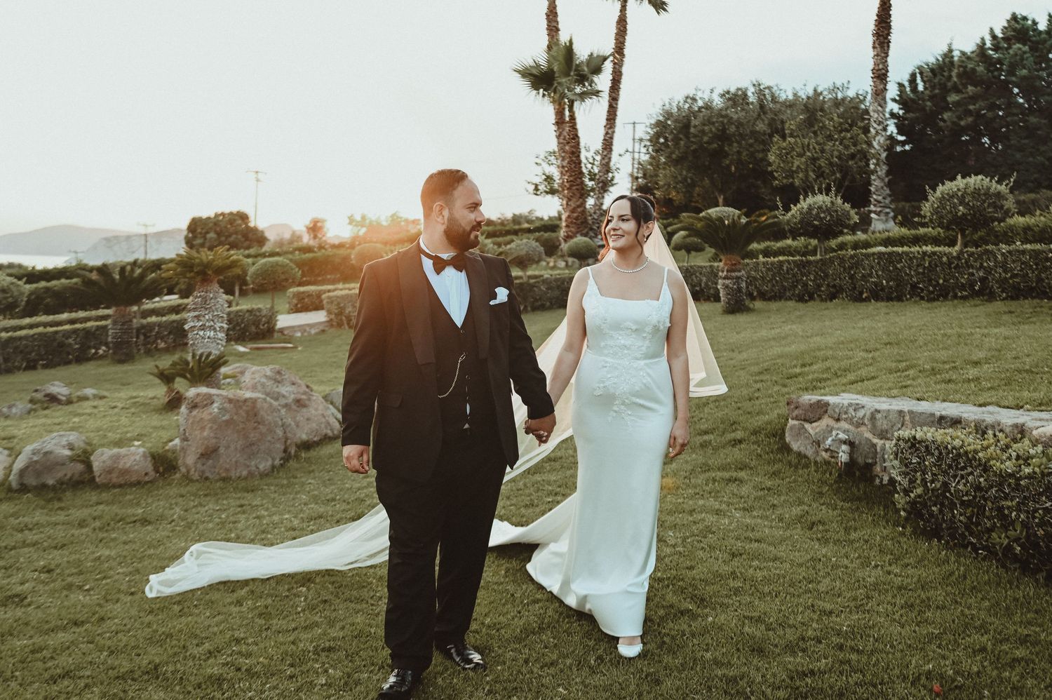 Black and white wedding photo of bride and groom gazing at each other outdoors among trees.
