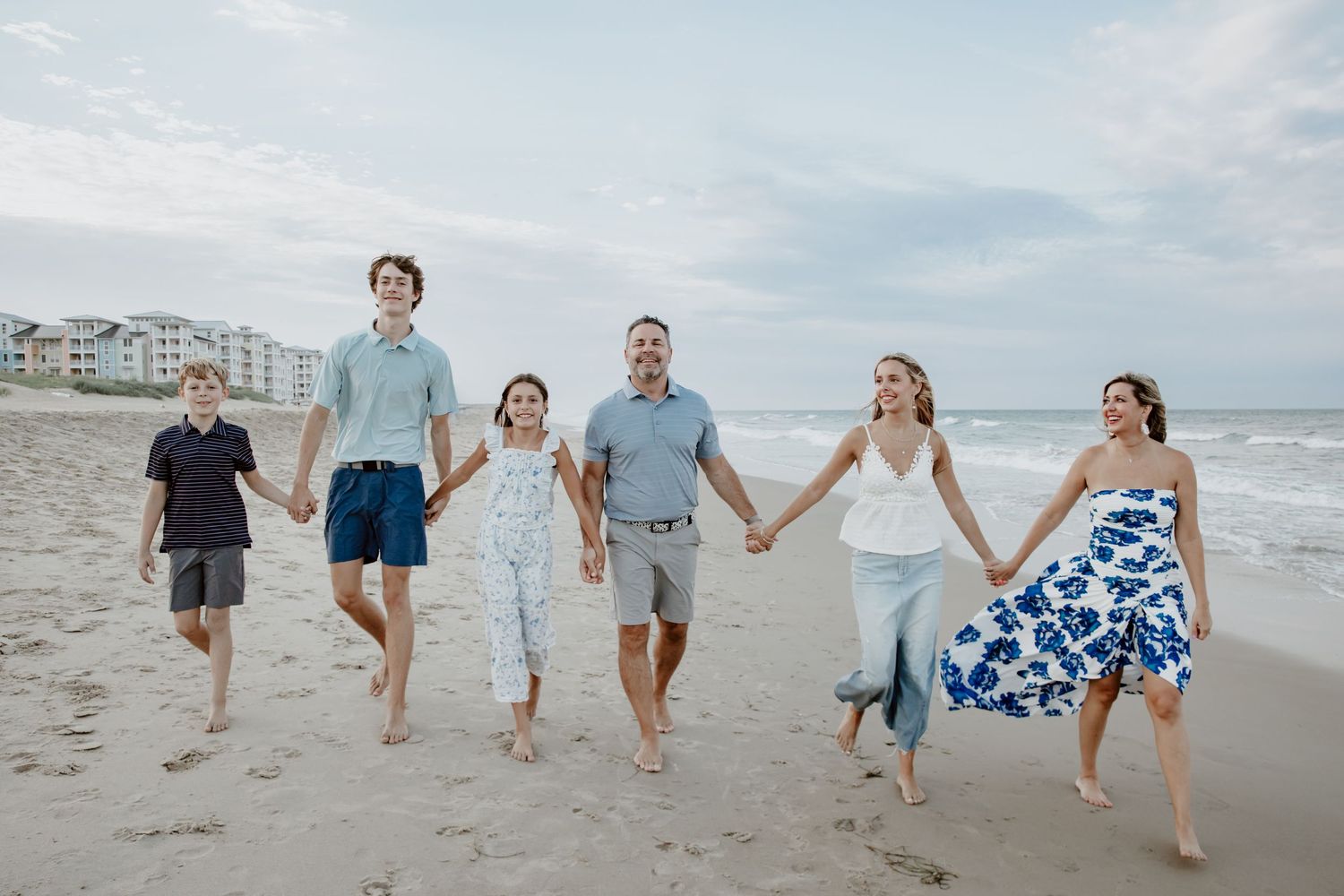Happy family of six walks hand-in-hand along a scenic ocean beach at sunset. Virginia Beach.