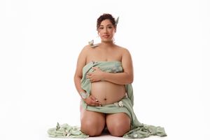 Expectant mother seated in mint lingerie with floral accents against a white background.