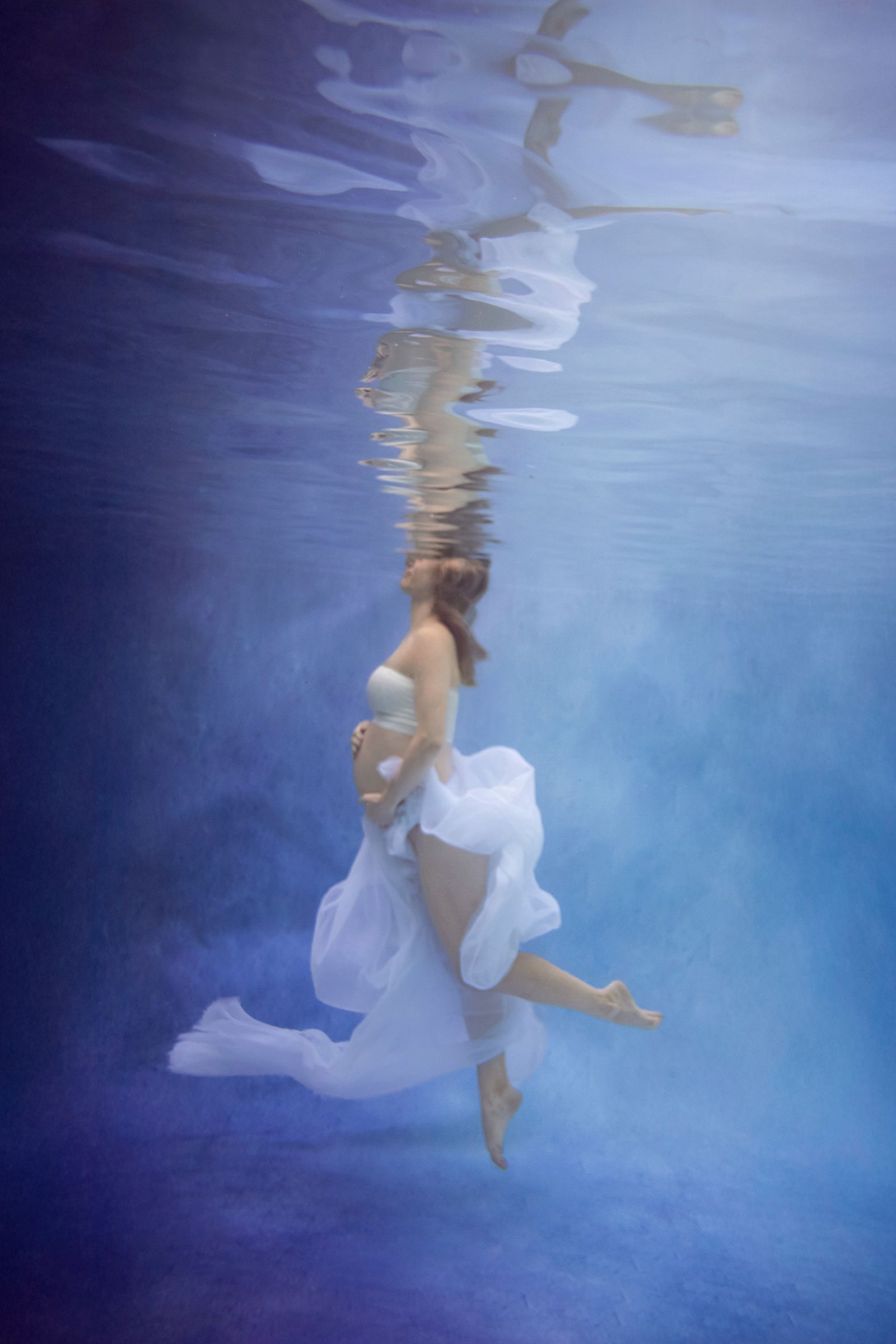 Expectant mother in a flowing blue gown with a mirrored reflection in a fine-art maternity portrait.
