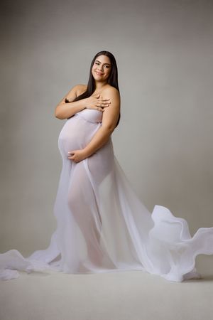 Expectant mother in a lavender gown with a long train, cradling her bump.