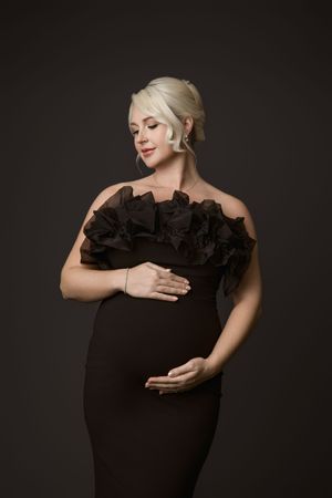Expectant mother in an off-the-shoulder black gown against a dark backdrop.