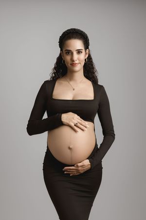Expectant mother in a black crop top and pants, cradling her bare baby bump.