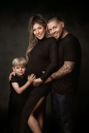 Expectant parents and their young child dressed in black for a family maternity portrait.