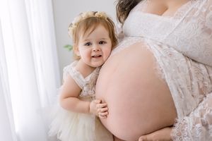 Young child kissing an expectant mother's bare bump in a tender maternity portrait.