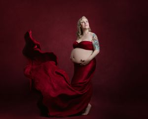 Expectant mother in a red gown surrounded by dramatic flowing fabric.