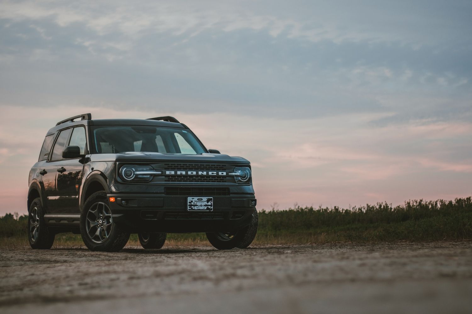 Black Ford Bronco silhouetted against a dramatic sunset sky on dusty terrain.