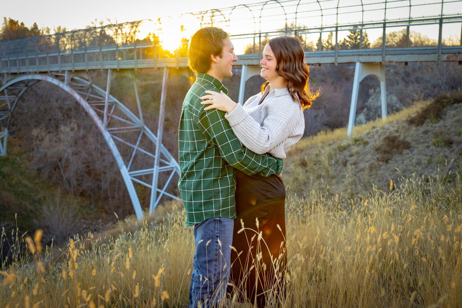a couple holding each other and laughing in front of a bridge at sunset.Family lifestyle session in Alberta by Creation Photography