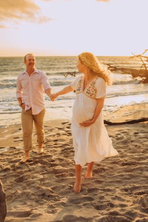 Couple walking on beach at sunset with flowing dress and romantic atmosphere.