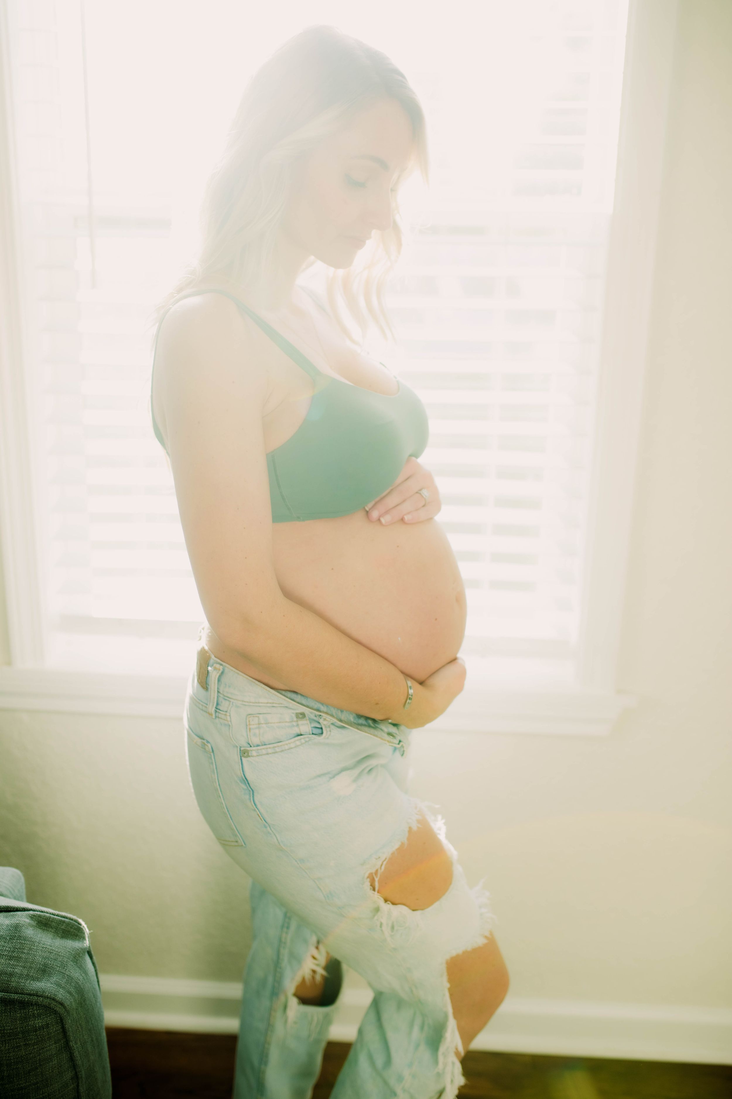 Side view of pregnant woman in casual wear by window in soft light.
