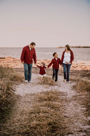 A family in matching red plaid shirts walks together on a coastal path during sunset.