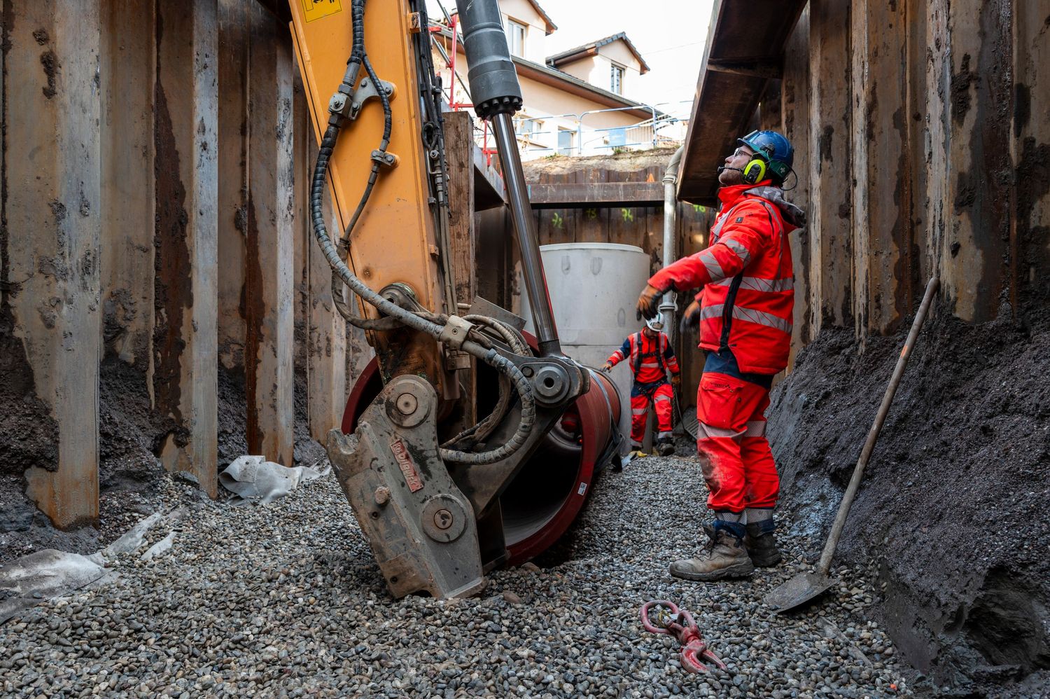 Construction workers in safety gear observe excavator loading dirt into dump truck at earthwork construction site.