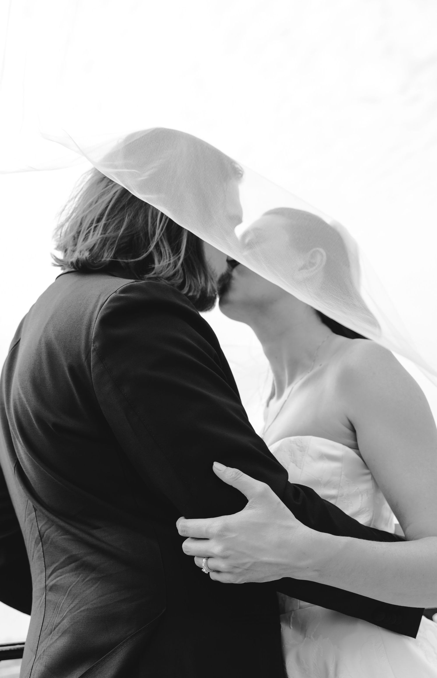 Romantic wedding photo of couple embracing in garden setting with bride holding floral bouquet.